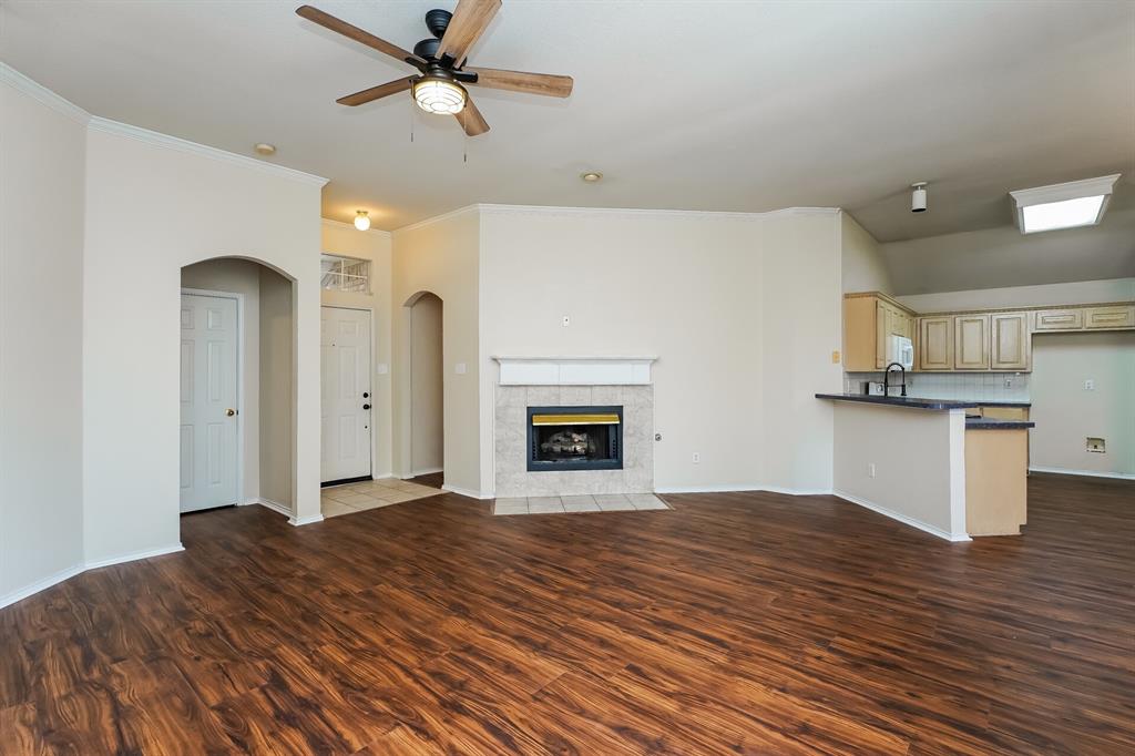 10706 Robincreek Lane Frisco, TX 75035 - Photo 2 of 17 Unfurnished living room featuring dark wood-type flooring, a tiled fireplace, arched walkways, ceiling fan, and ornamental molding