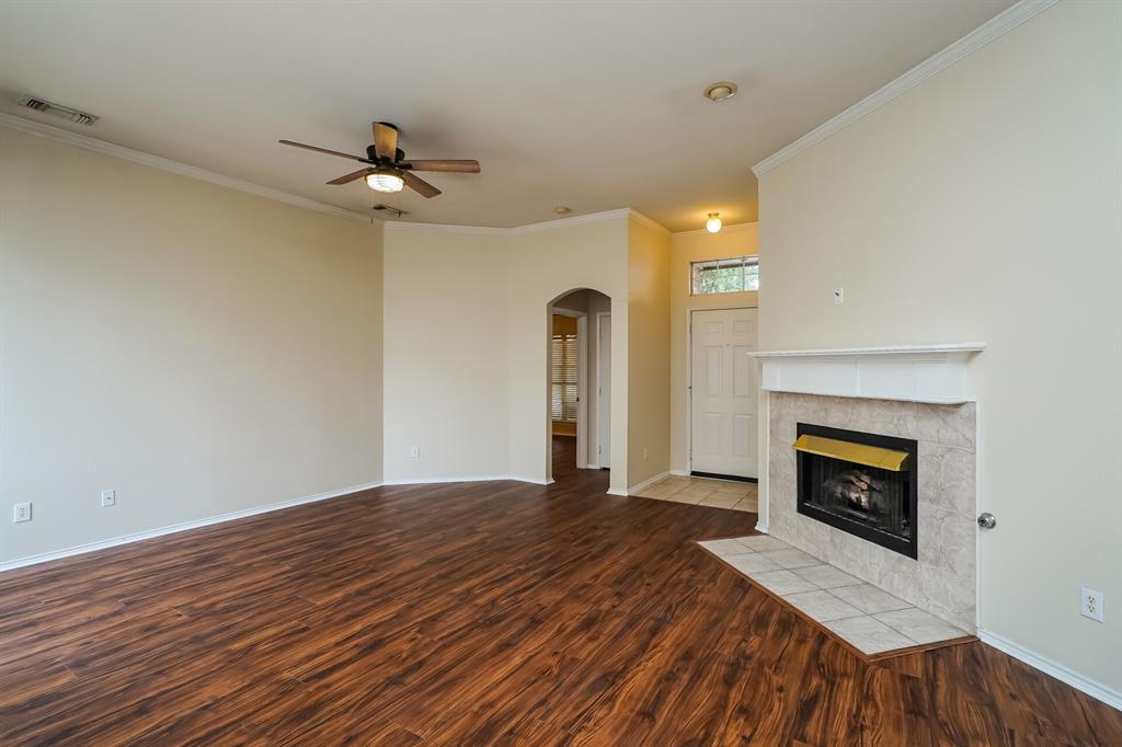 10706 Robincreek Lane Frisco, TX 75035 - Photo 4 of 17 Unfurnished living room with arched walkways, a tiled fireplace, dark wood-type flooring, crown molding, and a ceiling fan