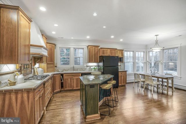 a kitchen with stainless steel appliances kitchen island granite countertop a refrigerator a stove a sink a dining table and chairs with wooden floor