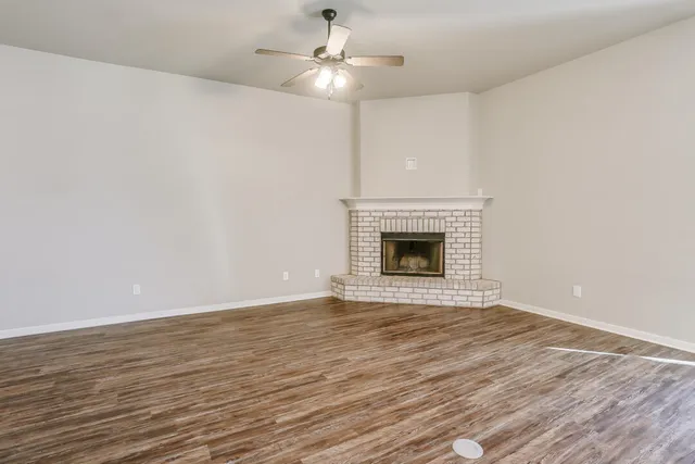 a view of an empty room with wooden floor fireplace and a window
