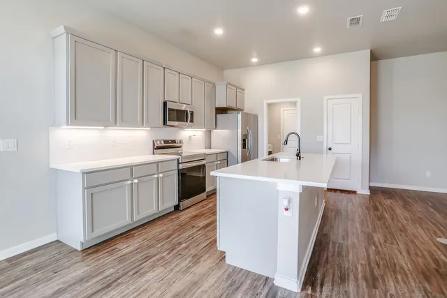 a kitchen with sink a microwave oven a refrigerator and white cabinets with wooden floor