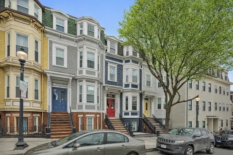 a front view of a building with lot of cars and trees