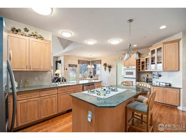 a kitchen with stainless steel appliances kitchen island granite countertop a refrigerator a stove a sink dishwasher and a dining table with wooden floor
