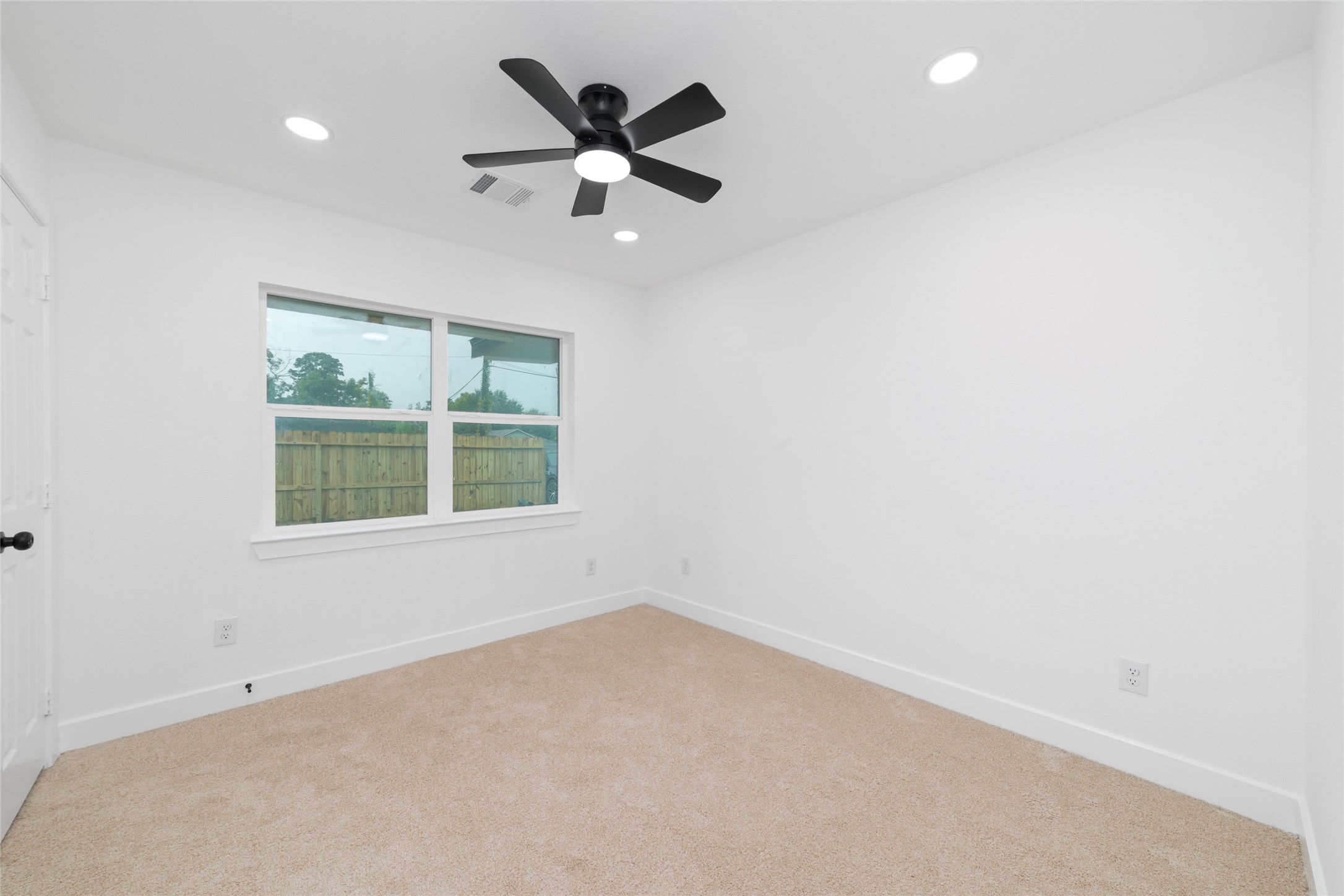 5709 Langley Road Houston, TX 77016 - Photo 18 of 27 This secondary Bedroom features neutral carpeting, white walls, and a ceiling fan with downlights. A window provides natural light and a view of the fenced yard, making it a bright, versatile space.