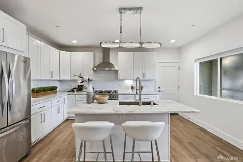 a kitchen with stainless steel appliances a sink stove a refrigerator and white cabinets with wooden floor