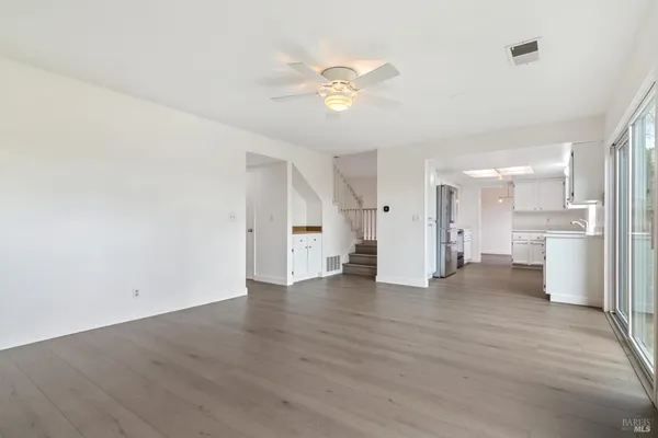 a view of an empty room with wooden floor and a kitchen