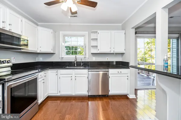 a kitchen with stainless steel appliances granite countertop a stove a sink and white cabinets with wooden floor