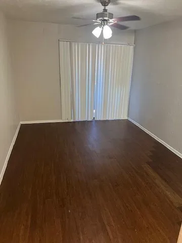 an empty room with wooden floor chandelier fan and windows