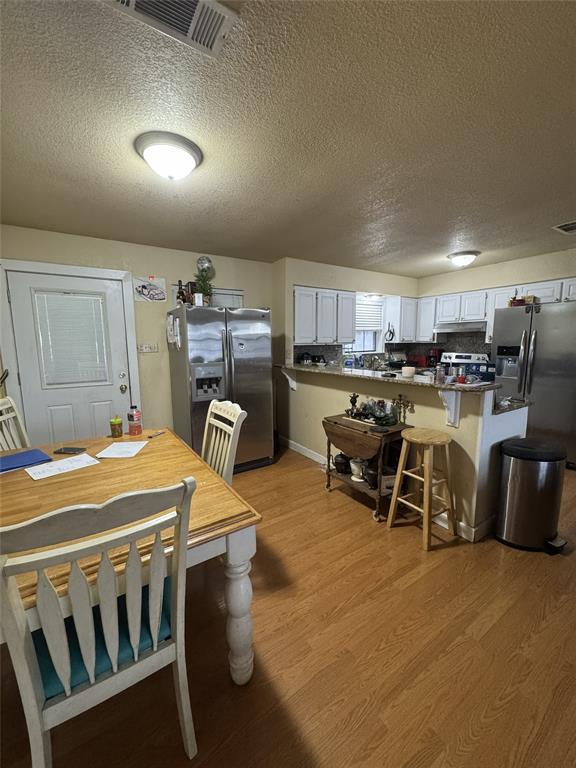 636 East Kempner Street Mabank, TX 75147 - Photo 11 of 28 Open-concept kitchen and dining area featuring wood-finish flooring, white cabinetry, and stainless steel appliances