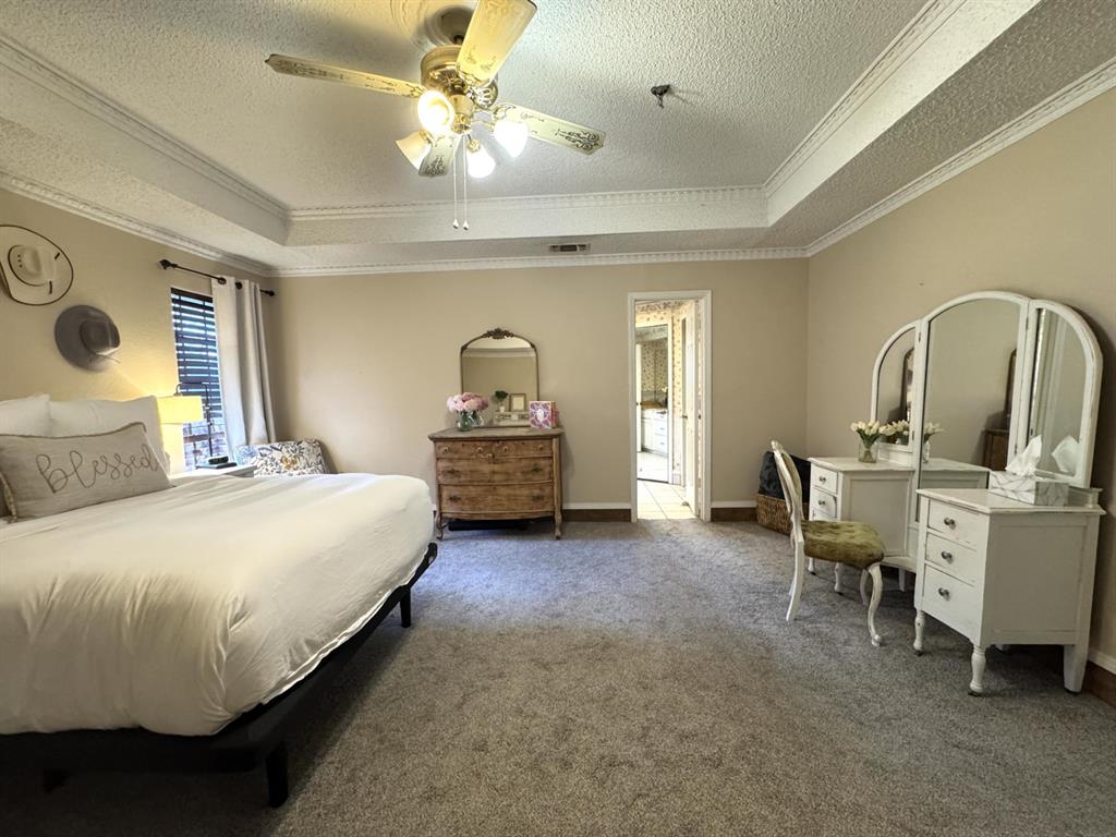 113 Northeast Timber Ridge Drive Burleson, TX 76028 - Photo 22 of 36 Spacious Primary Bedroom features Ensuite Bath, tray ceilings with detailed crown molding, a ceiling fan with integrated lighting, and neutral tone carpeting