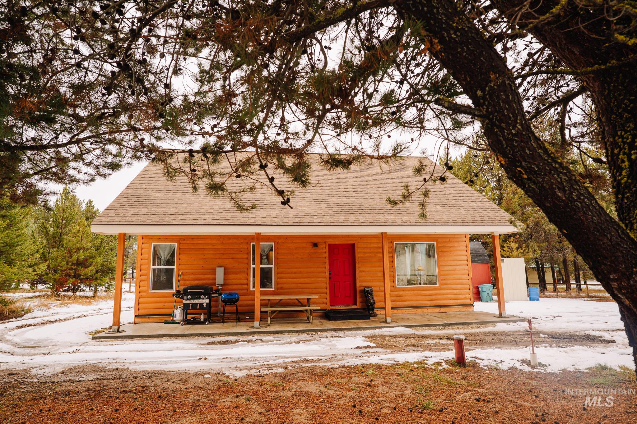 Snow covered house with a shingled roof, faux log siding, and a patio