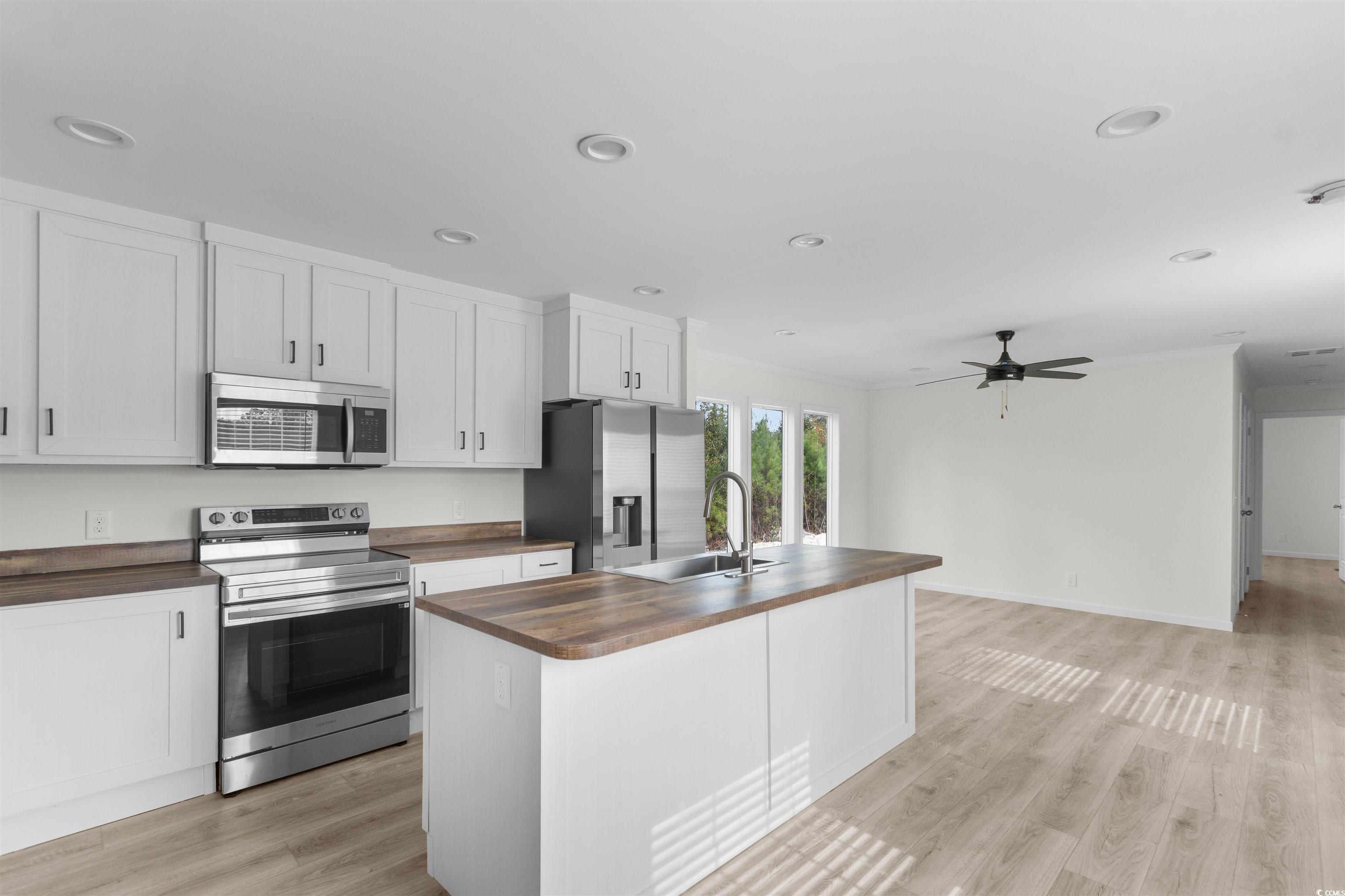 141 Feather Drive Georgetown, SC 29440 - Photo 11 of 34 Kitchen with stainless steel appliances, white cabinets, light wood finished floors, a center island with sink, and ornamental molding