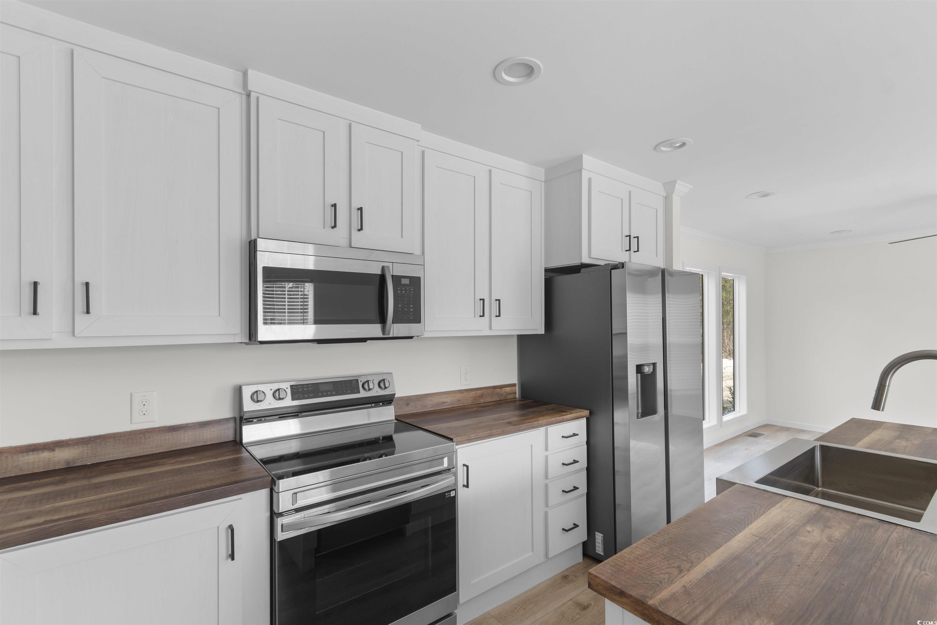 141 Feather Drive Georgetown, SC 29440 - Photo 12 of 34 Kitchen featuring stainless steel appliances, butcher block countertops, white cabinetry, crown molding, and light wood-style flooring