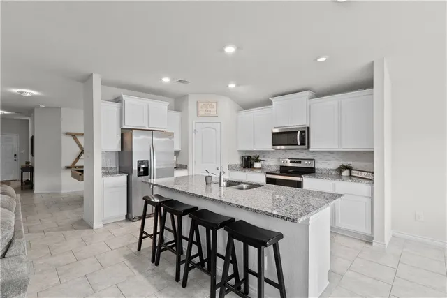a kitchen with stainless steel appliances granite countertop a stove top oven a sink a refrigerator and white cabinets