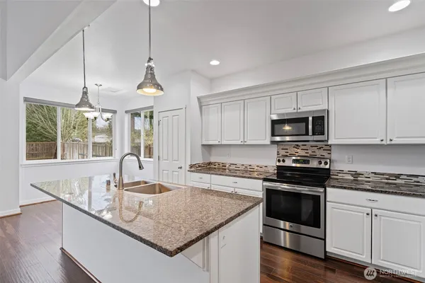 a kitchen with stainless steel appliances granite countertop a sink a stove and a wooden floors