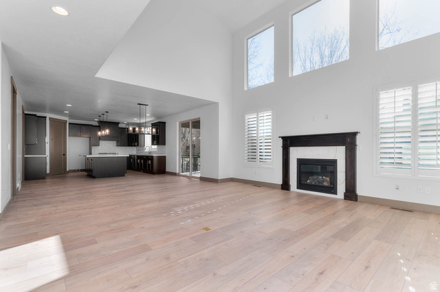 2724 Mt Jordan Road Sandy, UT 84092 - Photo 12 of 33 Unfurnished living room featuring a tile fireplace, light wood-style flooring, recessed lighting, and a high ceiling