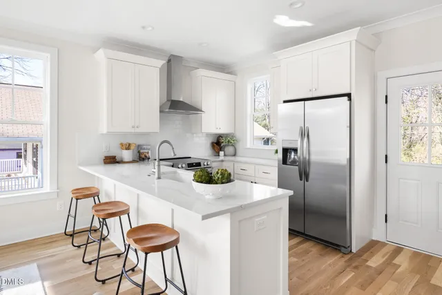 a kitchen with stainless steel appliances a refrigerator a sink a stove and white cabinets with wooden floor