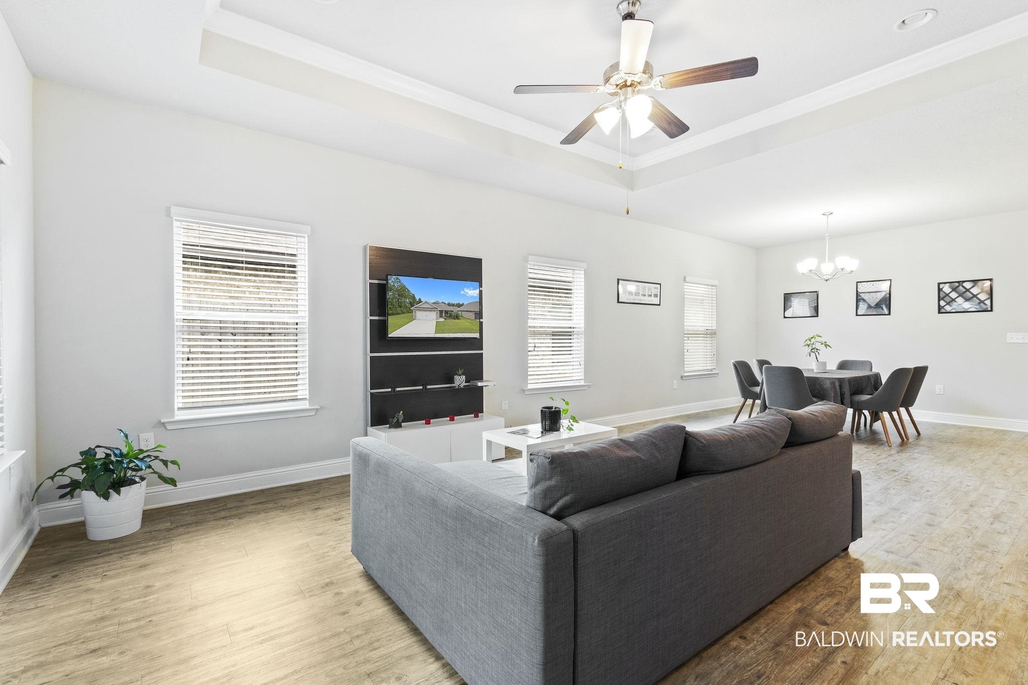 31643 Kestrel Loop Daphne, AL 36527 - Photo 8 of 59 Living room with hardwood / wood-style floors, ceiling fan with notable chandelier, a tray ceiling, and a healthy amount of sunlight