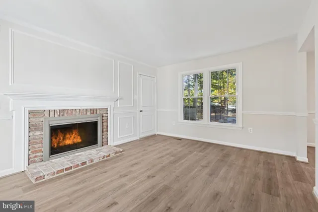 a view of an empty room with wooden floor fireplace and a window