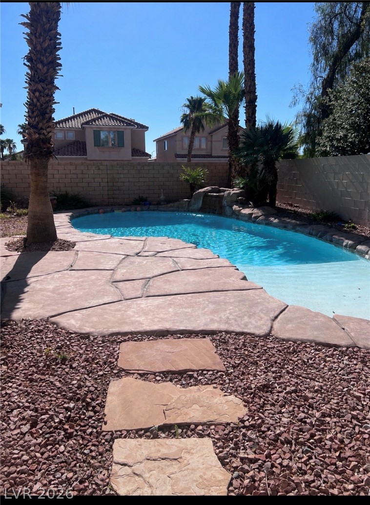 7815 Windward Road Las Vegas, NV 89147 - Photo 13 of 13 Palm trees shade a private pool lined with stone-patterned decking and a rock waterfall feature.
