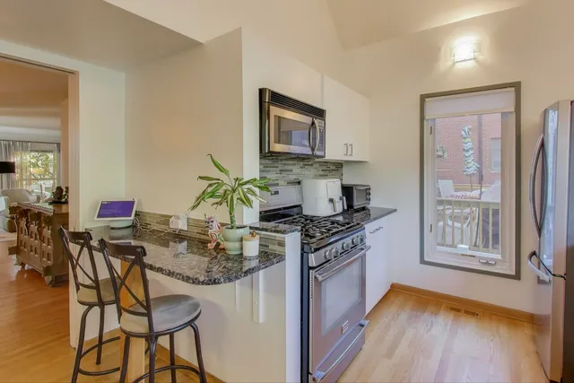 a kitchen with stainless steel appliances granite countertop a stove top oven a dining table and chairs with wooden floor