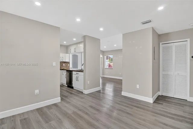 a view of an empty room with wooden floor and a kitchen