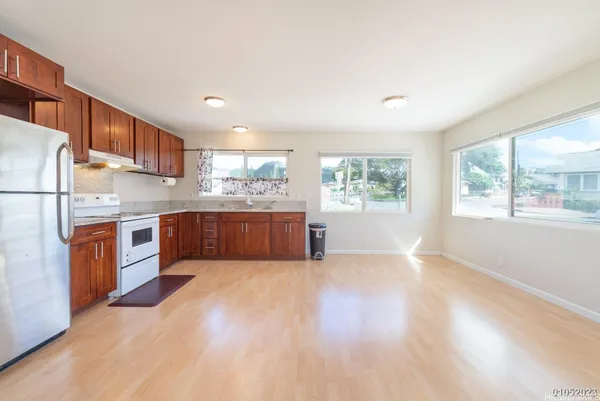 a kitchen with stainless steel appliances granite countertop a stove a sink dishwasher a refrigerator and white cabinets with wooden floor