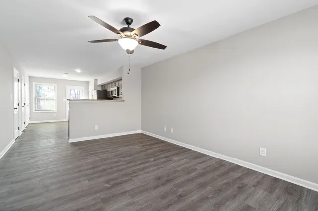a view of an empty room with wooden floor and a ceiling fan