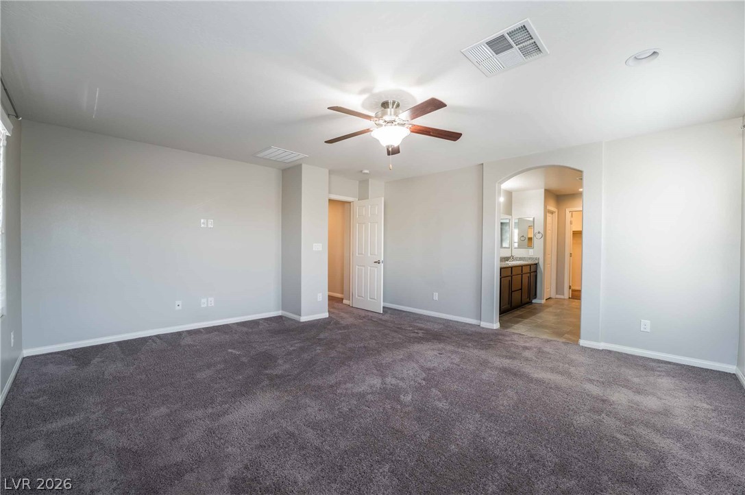 55 Canopus Ridge Way Las Vegas, NV 89183 - Photo 11 of 26 A spacious bedroom with a ceiling fan, plush carpeting, and an arched entry leading to an adjoining bath.