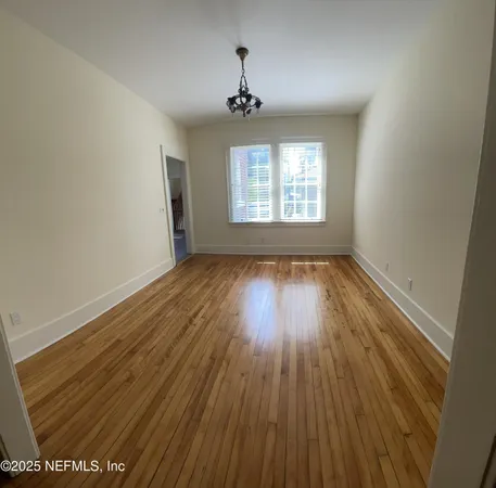 an empty room with wooden floor chandelier fan and windows
