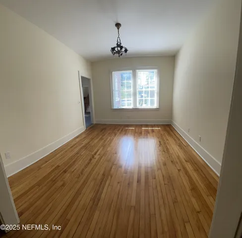 an empty room with wooden floor chandelier fan and windows