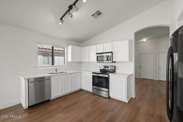 a kitchen with stainless steel appliances granite countertop a stove top oven a sink dishwasher a refrigerator and white cabinets with wooden floor