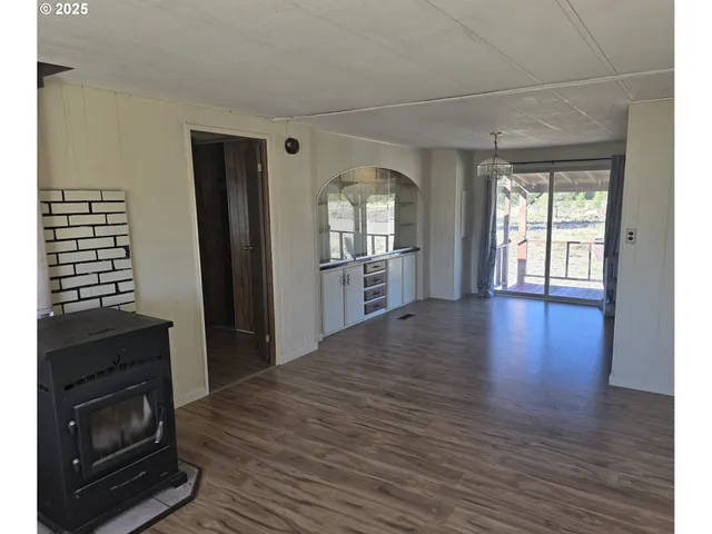 a view of a kitchen and an empty room with wooden floor and a window