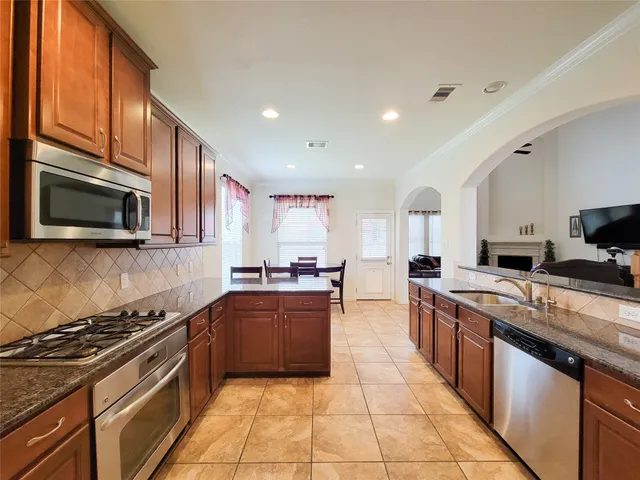 a large kitchen with stainless steel appliances granite countertop a stove top oven a sink dishwasher a dining table and chairs with wooden floor