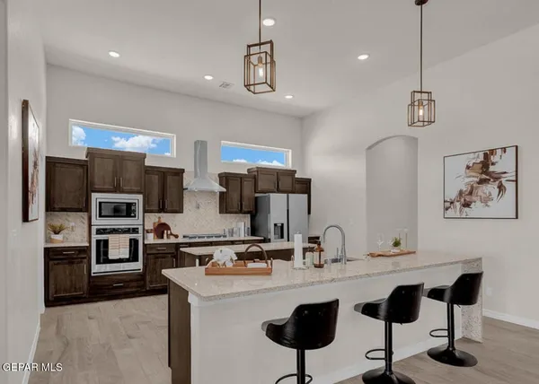 a kitchen with stainless steel appliances kitchen island granite countertop a sink a stove a refrigerator and island with wooden floor