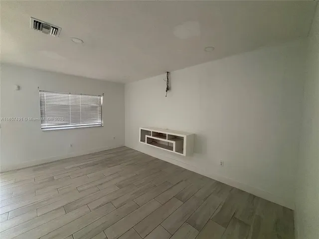 an empty room with wooden floor cabinet and windows