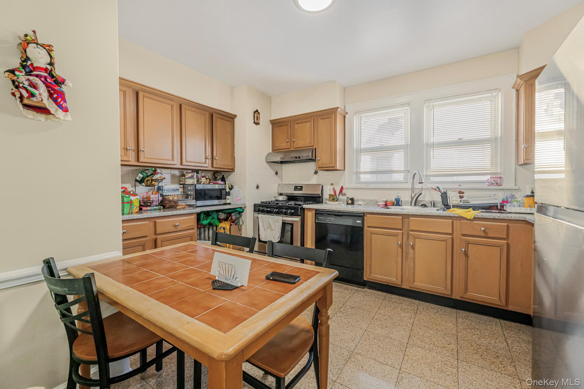 168 Stephenson Boulevard New Rochelle, NY 10801 - Photo 10 of 21 Kitchen featuring appliances with stainless steel finishes, brown cabinetry, under cabinet range hood, and light stone countertops