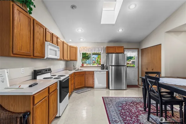 a kitchen with stainless steel appliances granite countertop a refrigerator a stove a sink a dining table and chairs with wooden floor