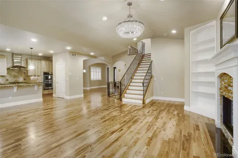 a view of an empty room with wooden floor kitchen view and a window