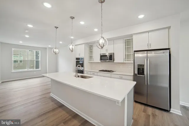 a kitchen with stainless steel appliances kitchen island granite countertop a refrigerator a sink dishwasher a stove and white cabinets with wooden floor