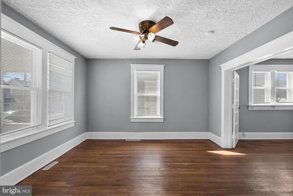 a view of an empty room with wooden floor and a ceiling fan