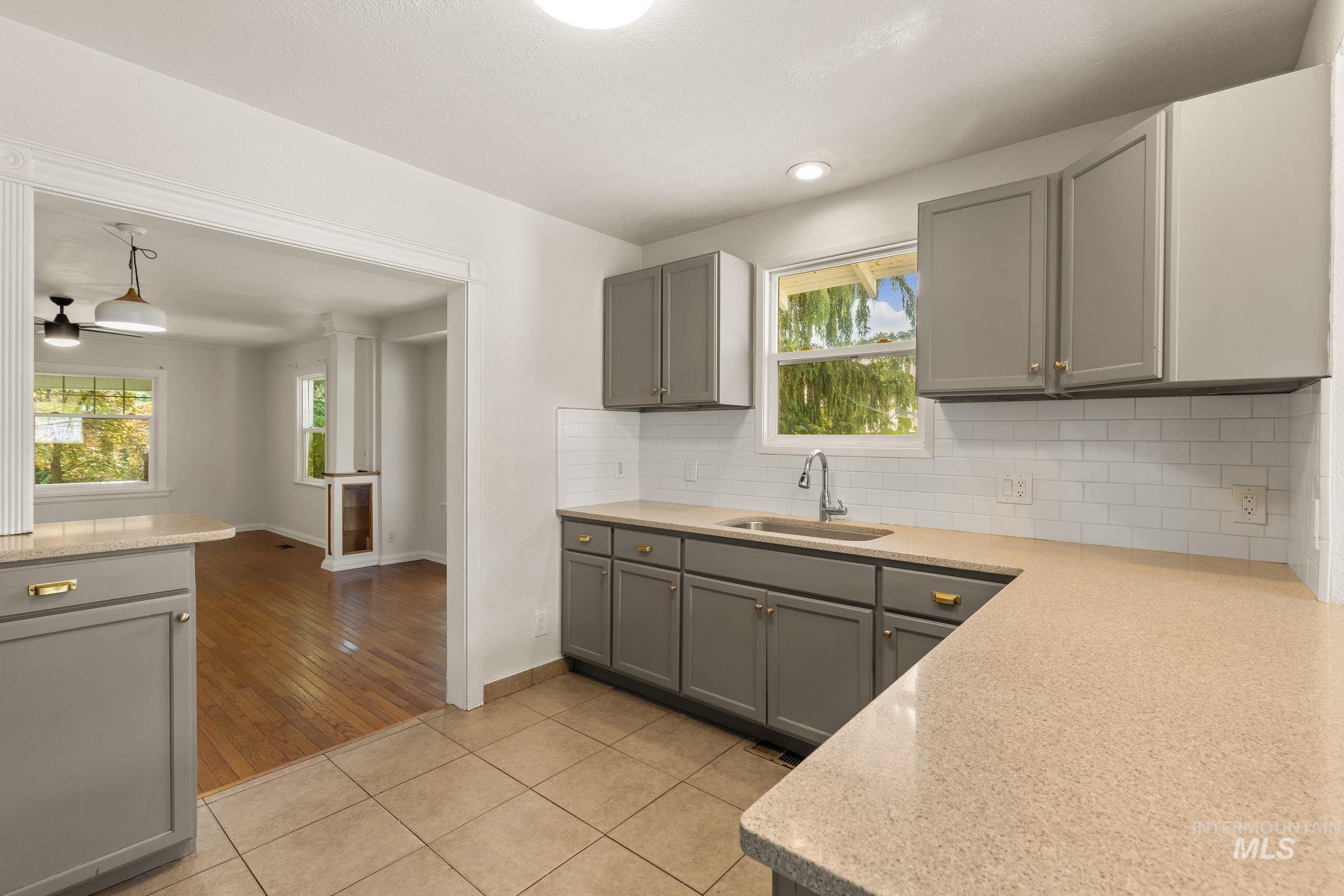 928 3rd Street Clarkston, WA 99403 - Photo 14 of 44 Kitchen featuring gray cabinetry with gold hardware, light-toned countertops, white subway tile backsplash, and a stainless steel sink with a modern faucet
