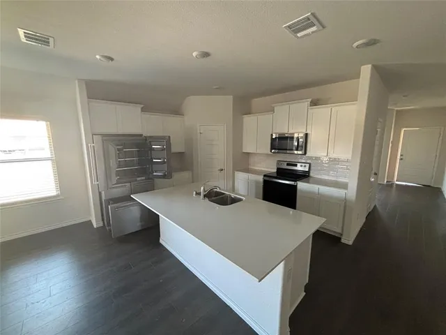 a kitchen with stainless steel appliances a stove a refrigerator a sink a stove and white cabinets with wooden floor