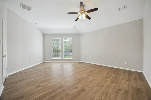 an empty room with wooden floor fan and windows