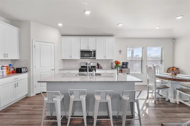 a kitchen with stainless steel appliances granite countertop a stove top oven a sink a refrigerator with white cabinets and wooden floor