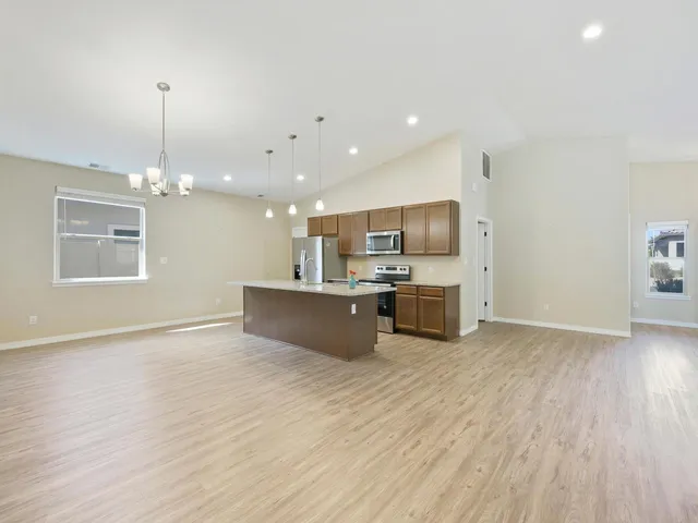 a large kitchen with stainless steel appliances a large counter top a stove a sink dishwasher and a refrigerator with wooden floor