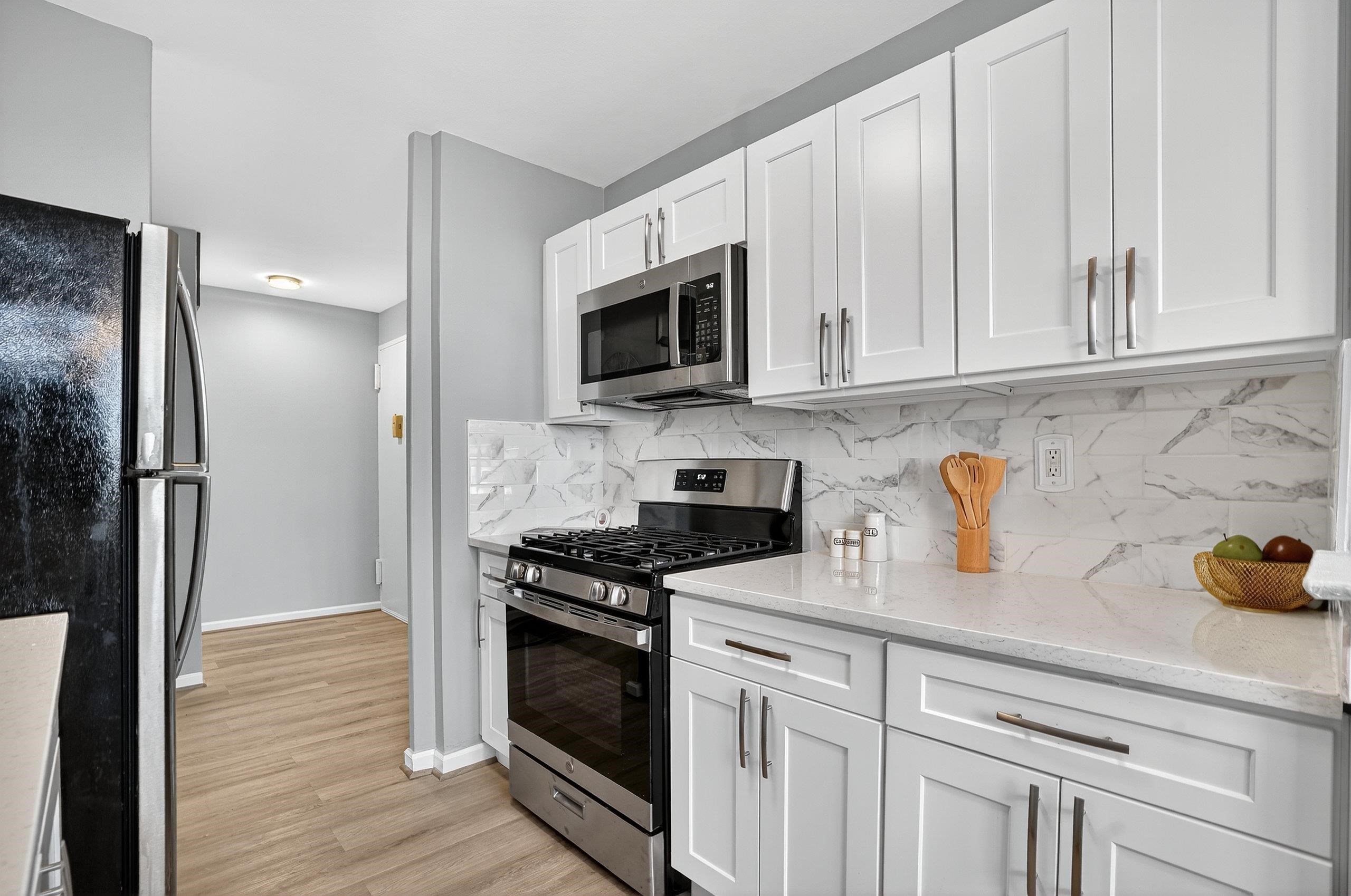 1225 John F. Kennedy Boulevard, Unit 12K Bayonne, NJ 07002 - Photo 5 of 18 a kitchen with cabinets stainless steel appliances and a wooden floor