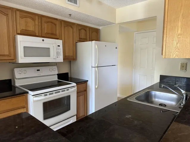 a kitchen with granite countertop white cabinets white stainless steel appliances and a refrigerator