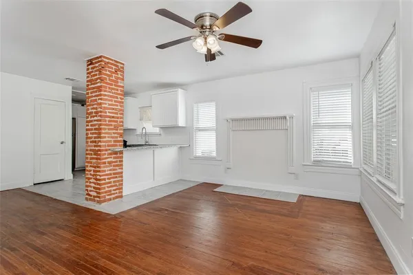 an empty room with wooden floor chandelier fan and windows