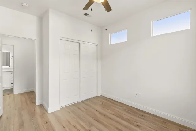 an empty room with wooden floor chandelier fan and windows